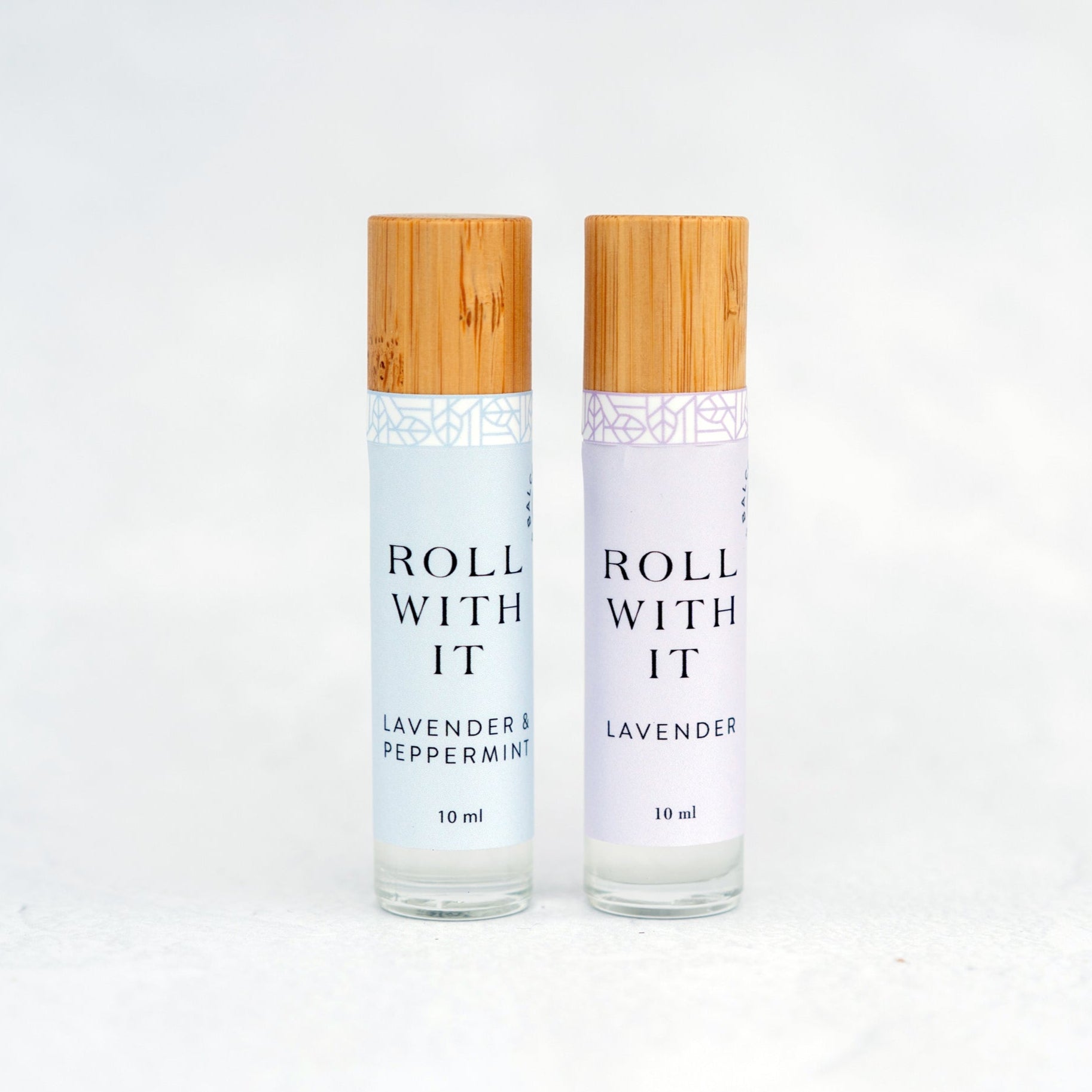 Two glass lavender aromatherapy roller bottles with bamboo caps on a white background